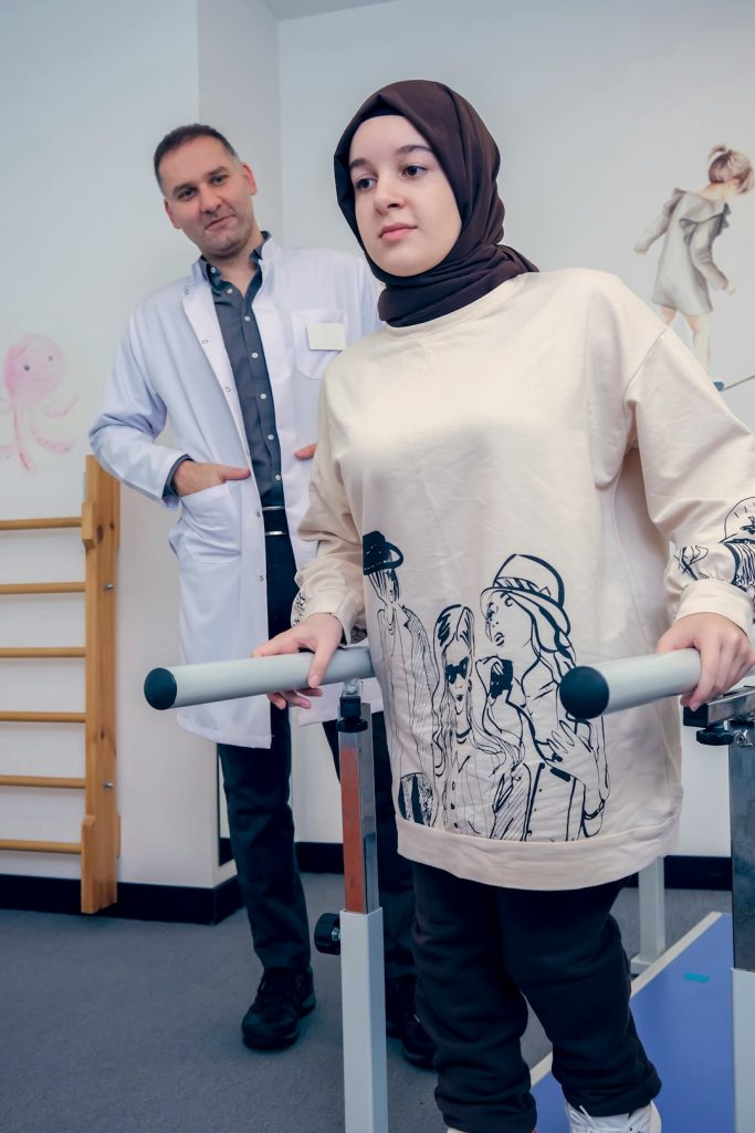 A child with arthrogryposis walks in the physiotherapy room with her doctor