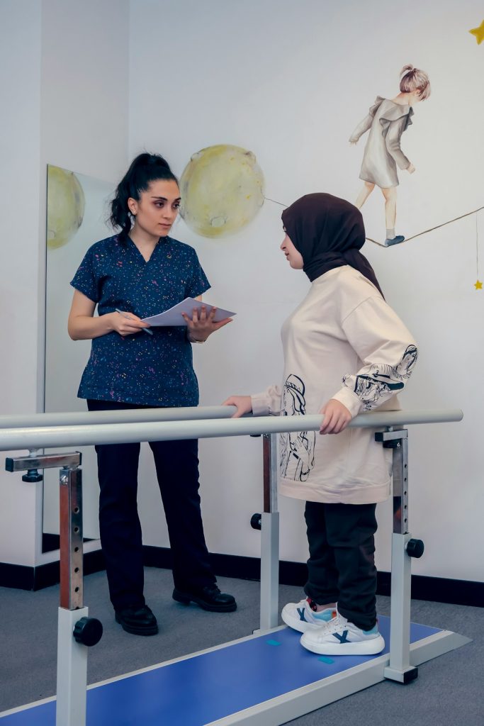 A child with arthrogryposis walks in the physiotherapy room, with the physiotherapist